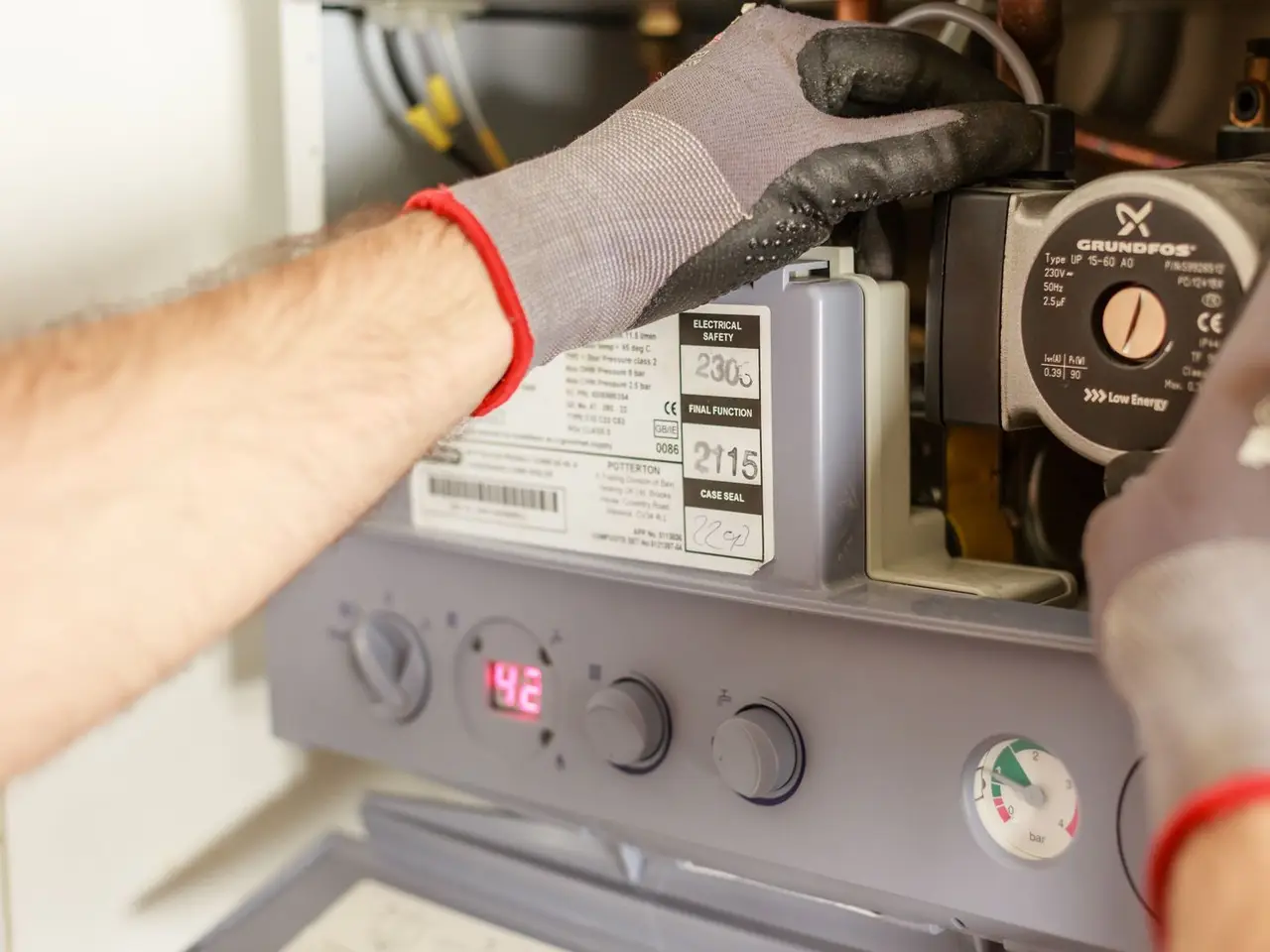 Technician in gloves working on a wall-mounted heater's controls
